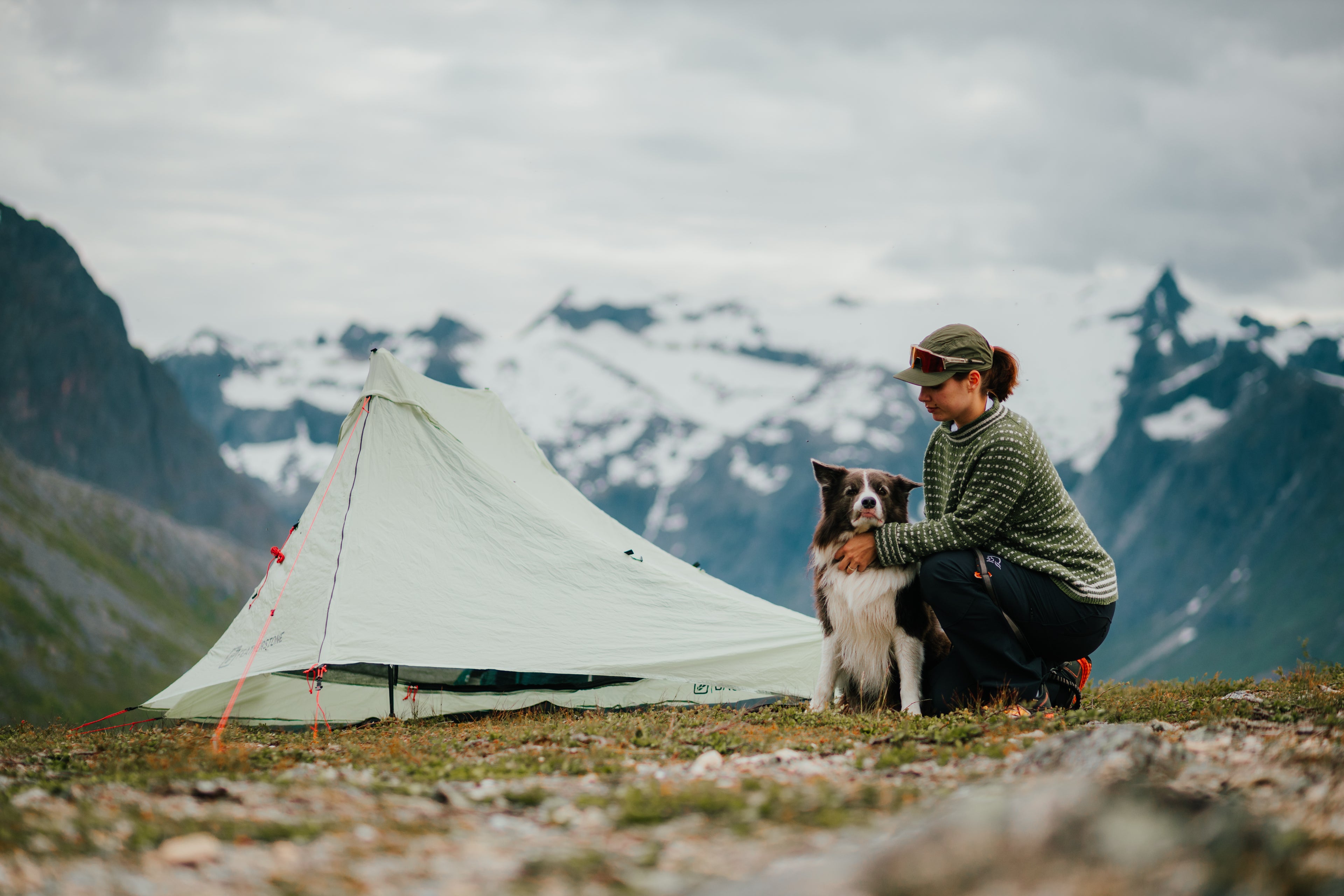 Person with a dog sitting in front of a tent in a mountainous landscape